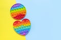 Popular silicone multi-colored anti-stress toy pop it in the shape of heart on yellow blue background flat lay top view. Trendy