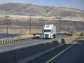 Popular white bi rig semi truck with dry van semi trailer climbing uphill on the winding highway road along Columbia River Royalty Free Stock Photo