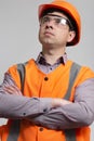 Young construction worker in hard hat and reflective vest with arms folded on the chest on grey studio background Royalty Free Stock Photo