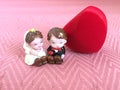 Porcelain bride and groom figurine dolls sitting together with heart shaped ring red gift box on pink background.