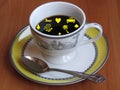 A porcelain cup of coffee, silver spoon and fortune telling pictures. White, grey and yellow cup on brown cherry wood background.
