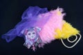 Porcelain mask lay on feathers covered by violet netting near pearl necklace on black background