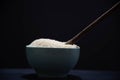 Porcelain pan with raw white rice and wooden spoon on black background Royalty Free Stock Photo