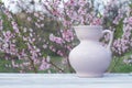 Porcelain pink jug on a table of white boards against the background of a flowering bush