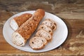 Sliced Integral Baguette Bread Elongated Loaf On White Porcelain Plate Set On Old Weathered Cracked Flaky Wooden Table