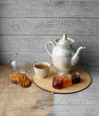 Porcelain tea kettle and teacup with green tea. Pressed roses on a wooden table. Three small jars of homemade berry jam on the woo Royalty Free Stock Photo