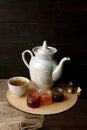 Porcelain tea kettle and teacup with green tea. Pressed roses on a wooden table. Three small jars of homemade berry jam on the woo Royalty Free Stock Photo