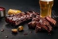 Pork ribs in barbecue sauce and a glass of beer on a black slate dish. A great snack to beer on a dark stone background Royalty Free Stock Photo