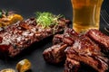 Pork ribs in barbecue sauce and a glass of beer on a black slate dish. A great snack to beer on a dark stone background Royalty Free Stock Photo