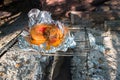 Pork leg meat in foil is heated on coals on a barbecue in nature. Background