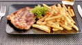 Pork neck with french fries on black plate