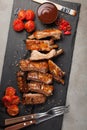 Pork ribs in barbecue sauce and honey roasted tomatoes on a black slate dish. A great snack to beer on a light stone table. Top vi Royalty Free Stock Photo