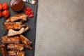 Pork ribs in barbecue sauce and honey roasted tomatoes on a black slate dish. A great snack to beer on a light stone Royalty Free Stock Photo