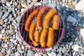 Pork sausages on portable bucket grill on stone beach Royalty Free Stock Photo