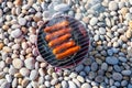 Pork sausages on portable bucket grill on stone beach Royalty Free Stock Photo