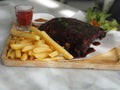 Pork Spareribs BBQ, Barbeque Pork Ribs with french fries vegetable salad, tomato sauce in a clear glass on wooden tray, food Royalty Free Stock Photo