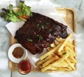 Pork Spareribs BBQ, Barbeque Pork Ribs with french fries vegetable salad, tomato sauce in a clear glass on wooden tray, food flat Royalty Free Stock Photo
