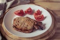 Pork steak and sliced tomato on a white plate on a wooden round tray Royalty Free Stock Photo