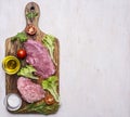 Pork steak with vegetables and herbs, meat knife and fork, on a cutting board oil and seasonings border ,place for text on Royalty Free Stock Photo