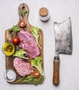 Pork steak with vegetables and herbs, meat knife and fork, on a cutting board with oil seasonings, and meat cleaver on wooden Royalty Free Stock Photo