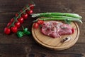 Pork steaks lie on a round cutting board next to fresh green asparagus and cherry tomatoes and a sprig of basil on a wooden table Royalty Free Stock Photo