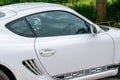 Porsche Cayman in white and black. Sporty German car with a green countryside background