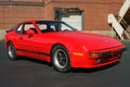 Porsche 944 in red in front of brick building