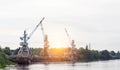 Port cranes with a bucket on the river bank, extraction of river sand, the sun Royalty Free Stock Photo