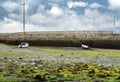 Port of Rianxo at low tide. Green algae and two anchored fishing boats in front of the wall under a gray cloudy sky Royalty Free Stock Photo