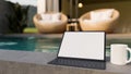 Portable digital tablet with wireless keyboard on stone pool coping over blurred swimming pool