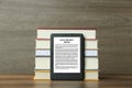 Portable e-book reader and stack of hardcover books on wooden table Royalty Free Stock Photo