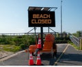 Portable electric digital sign by the a boardwalk ramp at the entrance to a beach that says, Beach Closed.