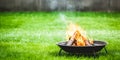 A portable fireplace with bright burning fire woods against grass background.