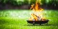 A portable fireplace with bright burning fire woods against grass background.