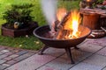 A portable fireplace with bright burning firewood making sparks and smoke at the backyard or garden near house. A place for eveni