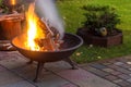 A portable fireplace with bright burning firewood making sparks and smoke at the backyard or garden near house. A place for eveni