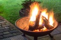 A portable fireplace with bright burning firewood making sparks and smoke at the backyard or garden near house. A place for eveni