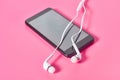 Portable white headphones and smartphone or tablet on pink background