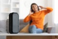 Portable wireless musical column standing on table, woman enjoying music