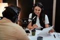 Portait of happy female radio host smiling, reading a script from paper while talking to male guest, presenter Royalty Free Stock Photo