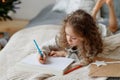 Portait of small lovely beautiful curly child draws pictures on blank white sheet of paper, wants to congratulate her