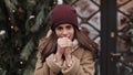 Portarait of cute brunnete caucasian girl in winter hat feeling cold, warming her hands, looking to camera, standing at