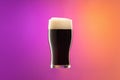 One full glass of frothy dark beer isolated over gradient purple and orange color background in neon. Concept of alcohol