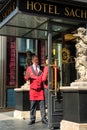 Porter in red uniform next to the sacher hotel door waiting guests