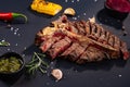 Porterhouse t-bone steak is grilled sliced on a piece with grilled corn, sauce, chilli, rosemary, salt, garlic on black background Royalty Free Stock Photo