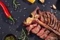 Porterhouse t-bone steak is grilled sliced on a piece with grilled corn, sauce, chilli, rosemary, salt, garlic on black background Royalty Free Stock Photo