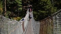 Porters crossing suspension bridge with Buddhist prayer flags spanning Dudhkoshi River near Manjo on Mount Everest Base Camp Trek.