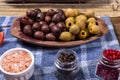 Portion of black, green olives, bowl with pink himalayan salt and glass jars with grains of red and black pepper Royalty Free Stock Photo