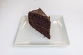 Portion of brownie with two layers of shortbread and glossy frosting on a square white porcelain plate