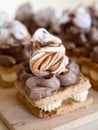 Portion cakes of meringue and cocoa butter cream in square form on a wooden stand, a piece of cake on a light wooden